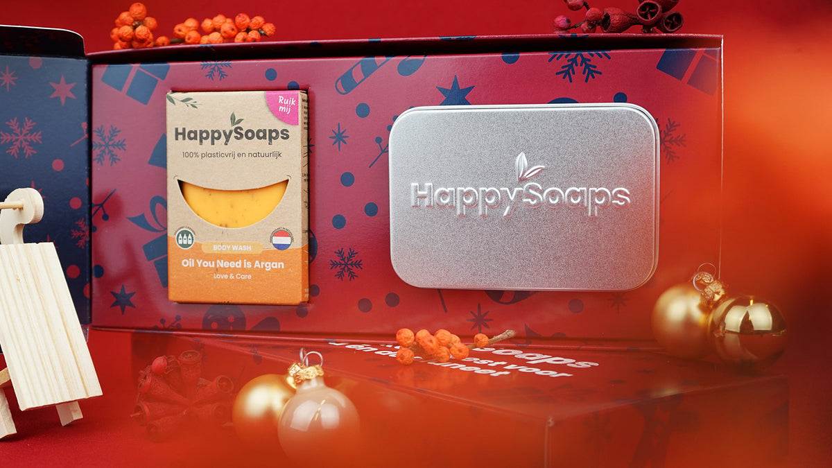Geopende Kerst Cadeau Giftbox met de Body Wash Bar Oil You Need is Argan en het rechthoekige reisblikje, tussen kerstballen en bessen