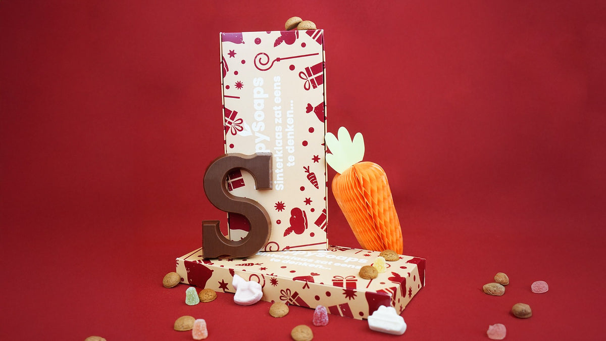 Sinterklaas Cadeau Giftbox rechtop op een rode achtergrond, met een chocoladeletter, een papieren wortel, pepernoten en snoepjes