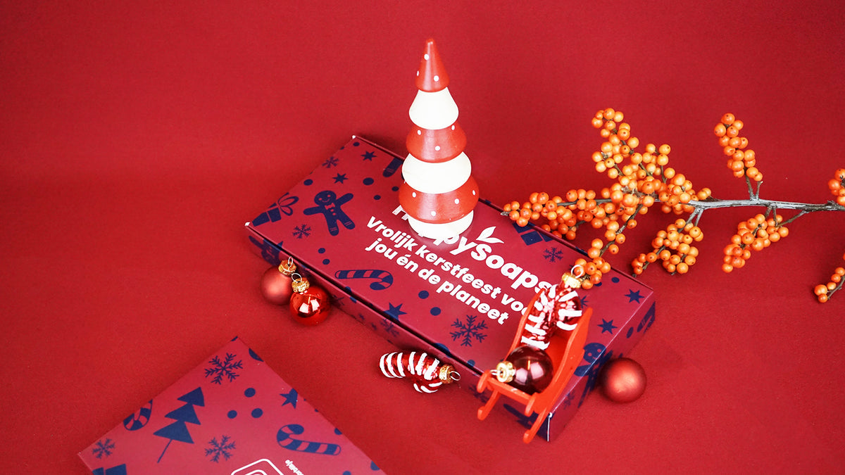 Kerst Cadeau Giftbox plat op rode stof, met een rood-wit kerstboompje, kerstballen en een kleine rode slee
