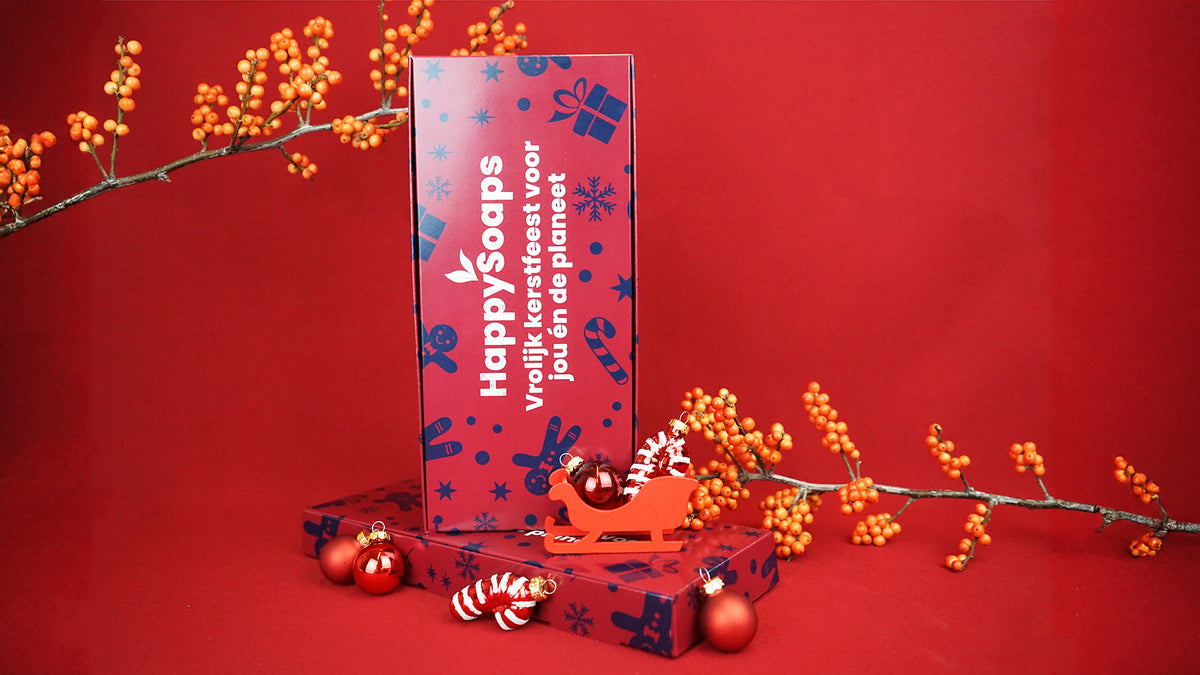 Kerst Cadeau Giftbox rechtop op een rode achtergrond, met een rode slee, kerstballen en oranje bessentakken