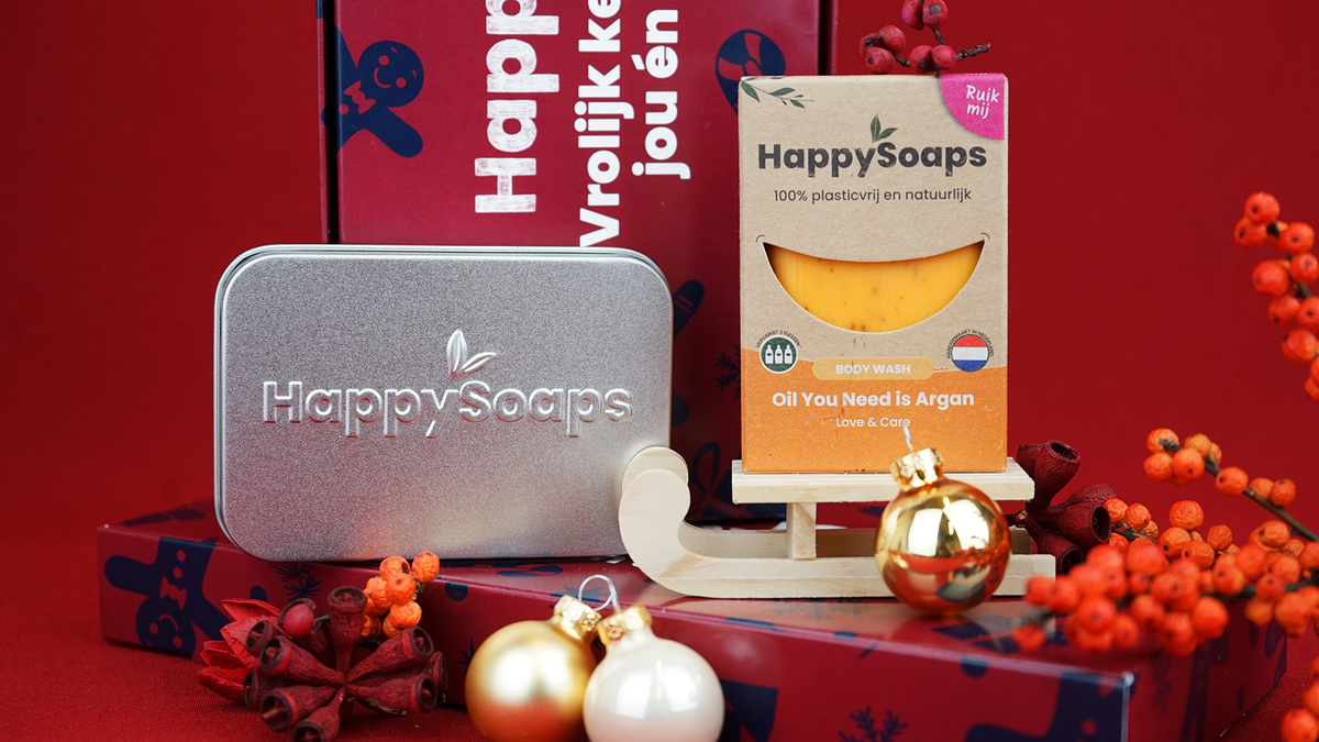 Het rechthoekige reisblikje en de Body Wash Bar Oil You Need is Argan op de Kerst Cadeau Giftbox, met gouden en witte kerstballen