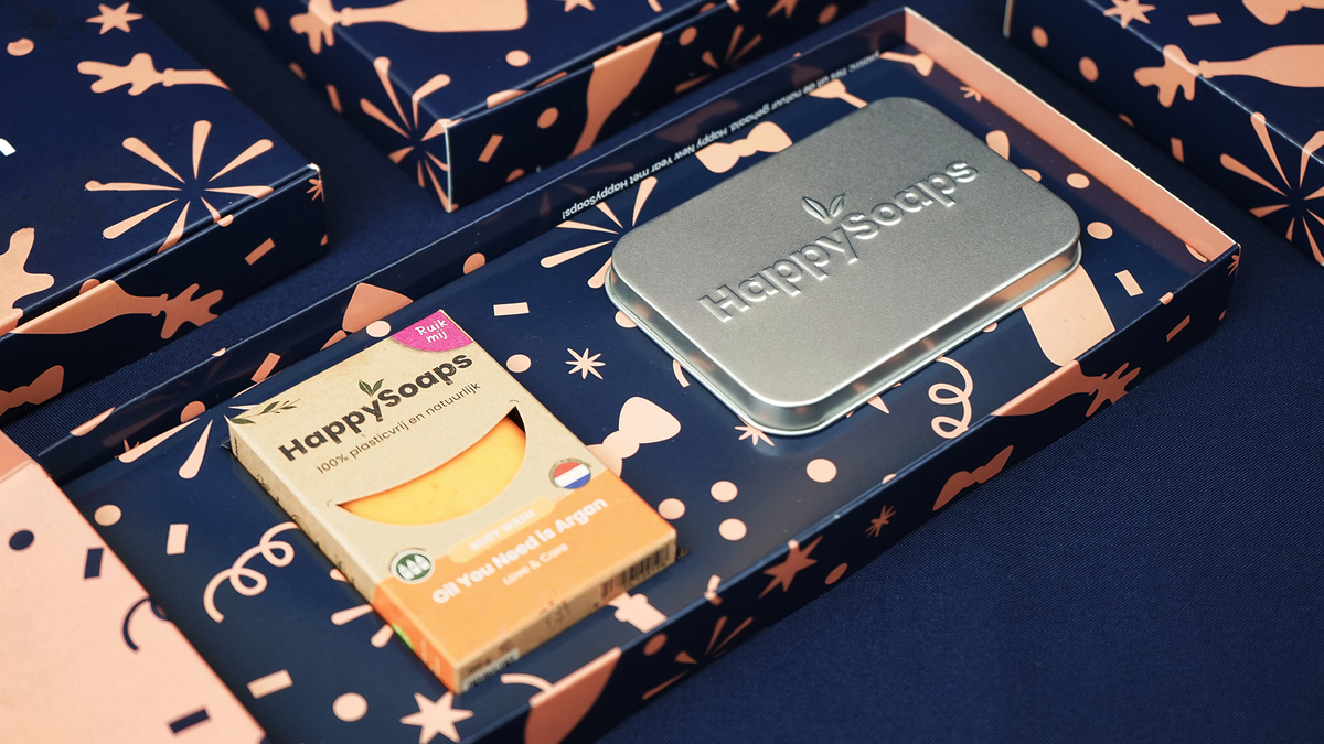 Inkijk in de Nieuwjaarscadeau Giftbox: de Body Wash Bar Oil You Need is Argan in de wikkel naast het reisblikje met HappySoaps-logo