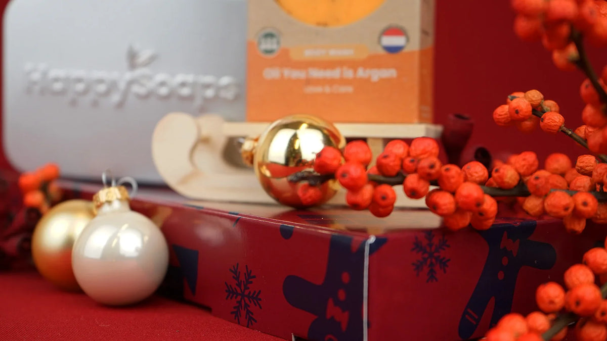 Kerst Cadeau Giftbox met het reisblikje en de Body Wash Bar, tussen gouden kerstballen, oranje bessen en een houten slee